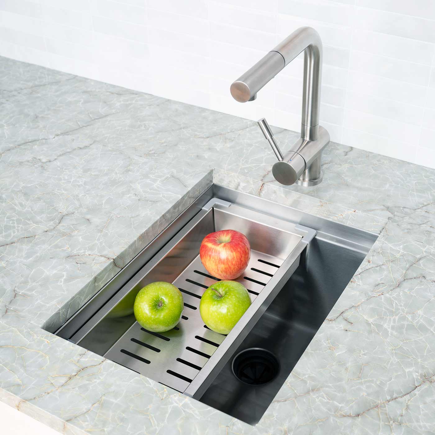 15-inch stainless steel workstation bar sink with an integrated drying rack holding fresh apples. A functional addition to any kitchen or bar.