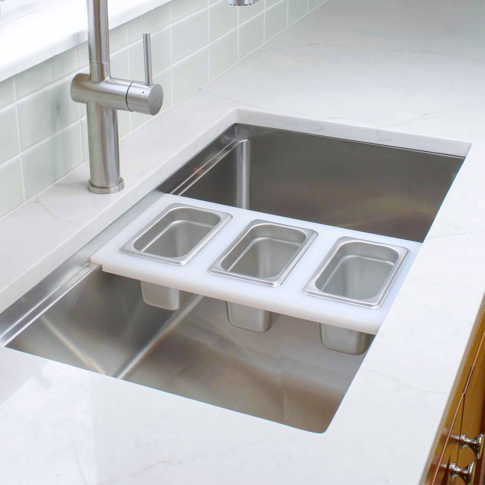 White plastic cutting board for workstation sink with stainless steel hotel pans and lids off