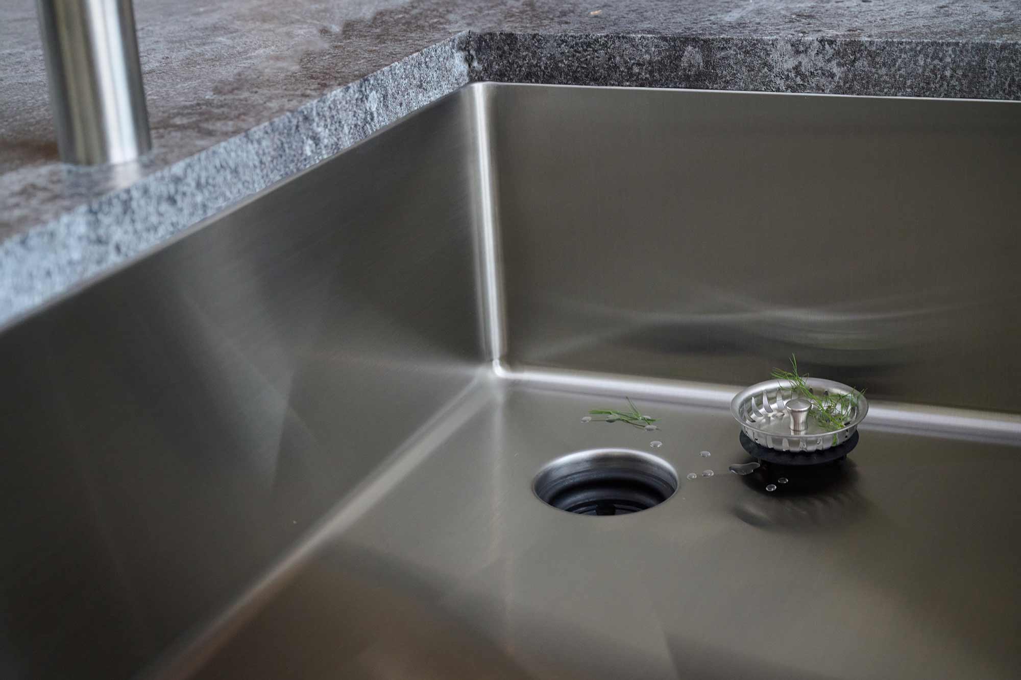 Close-up of stainless steel undermount sink with offset right drain, highlighting seamless construction and easy-to-clean 1/2-inch radius corners.