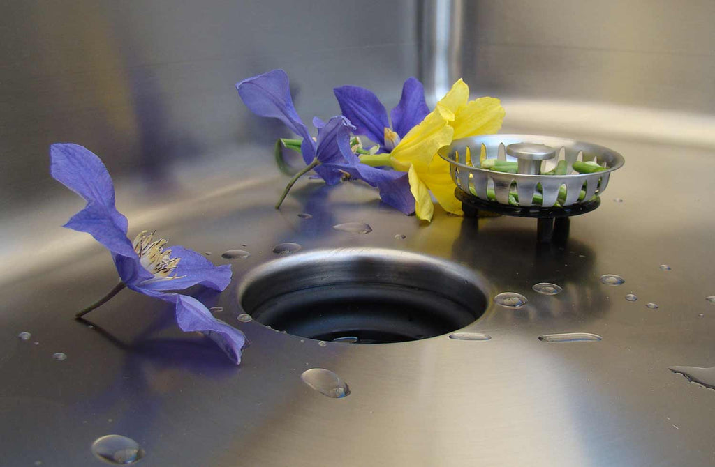 Close-up of a stainless steel sink with a Seamless Drain and Disposal Kit strainer basket, highlighting its sleek and functional design.