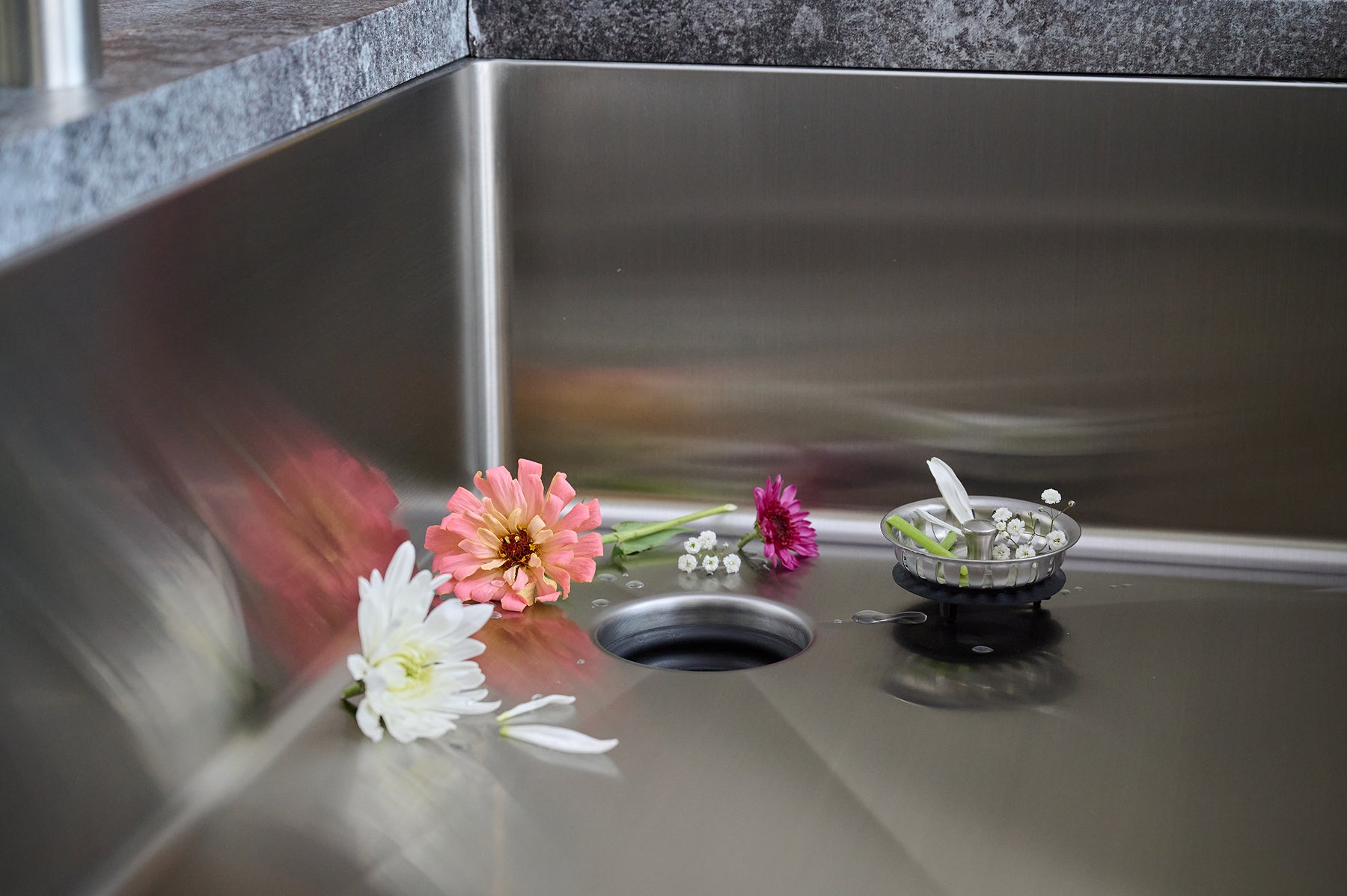 Close-up of the Seamless Centerpiece Drain in a Create Good Sinks stainless steel basin with fresh flowers and a strainer basket