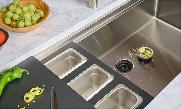 Stainless steel workstation kitchen sink with Seamless Centerpiece Drain, cutting board and stainless prep containers on the ledge