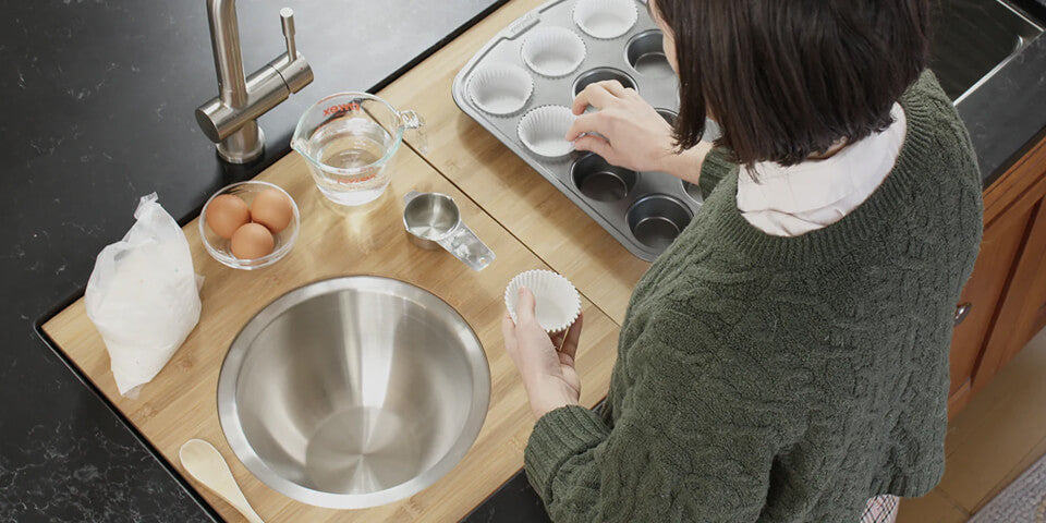 Person baking at a workstation sink covered with bamboo cutting boards and a stainless steel mixing bowl set into the ledge