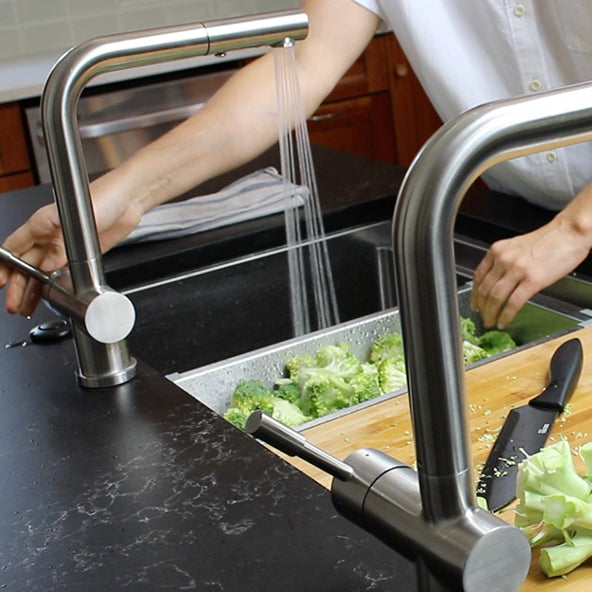 Close-up of the Ardell Stainless Steel Kitchen Faucet with its pull-out spout in action, rinsing fresh broccoli in a modern kitchen sink.