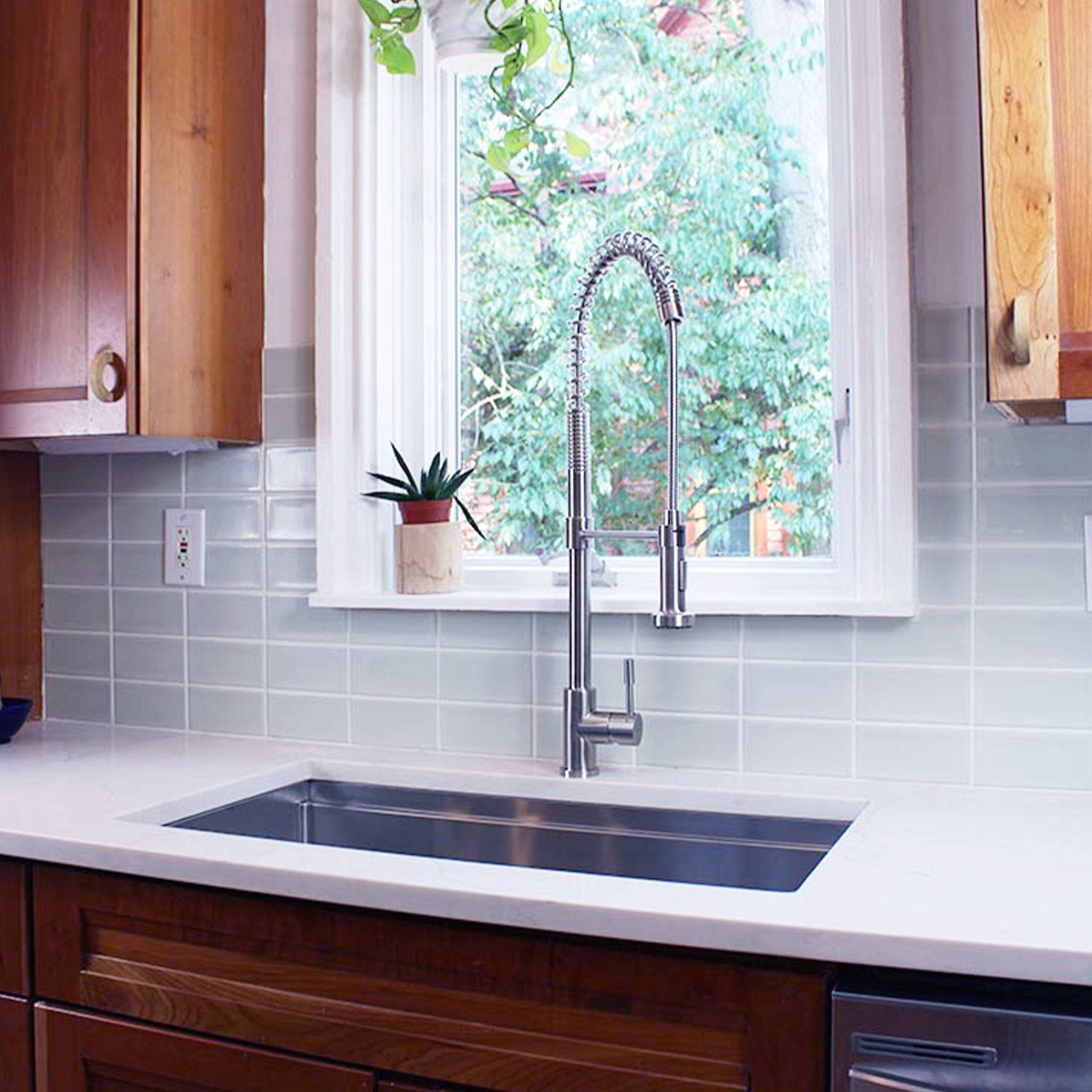 Jerry kitchen sink faucet in brushed stainless steel, mounted on a white countertop with a subway tile backsplash and wooden cabinetry.
