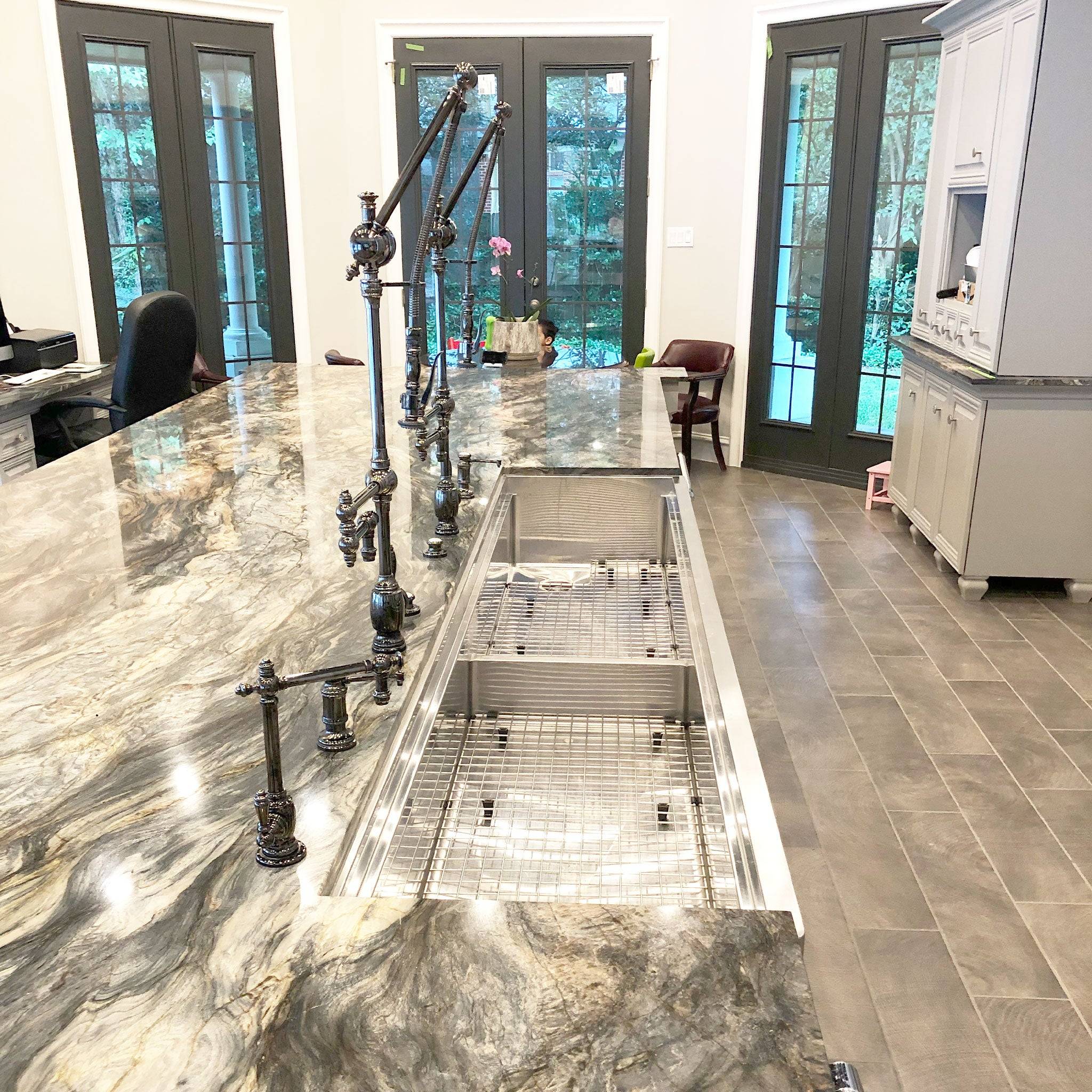 Expansive 84-inch stainless steel apron front sink installed in a luxury kitchen with marble countertops and industrial-style faucets.