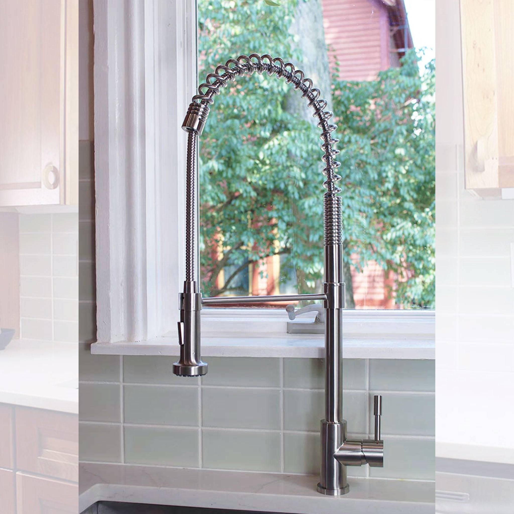 Close-up of the Jerry stainless steel kitchen faucet with a flexible spring spout, installed in front of a window with a green outdoor view.