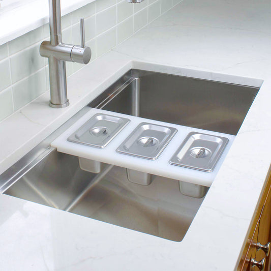 White plastic cutting board for workstation sink with stainless steel hotel pans and lids for condiments or garnish station