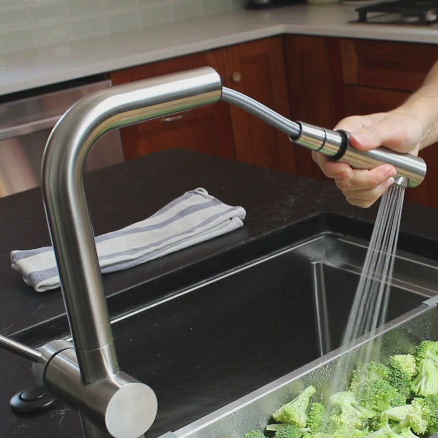 Close-up of the Ardell Stainless Steel Kitchen Faucet with its pull-out spout in action, rinsing fresh broccoli in a modern kitchen sink.